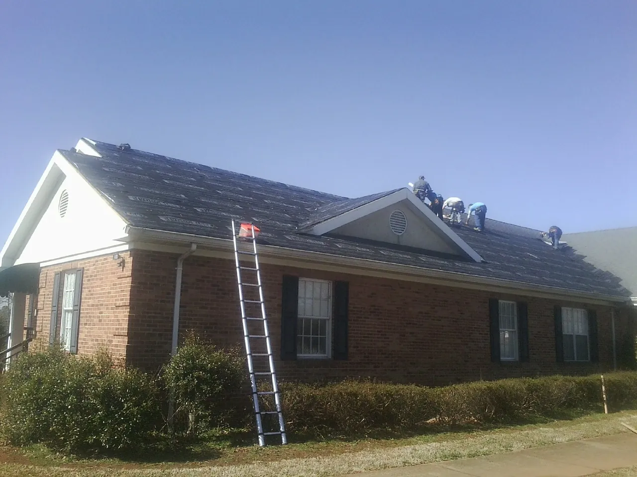 Crew tearing shingles off a brick ranch roof with a ladder set — Emergency Roof Repair work by our crew in Mount Gilead