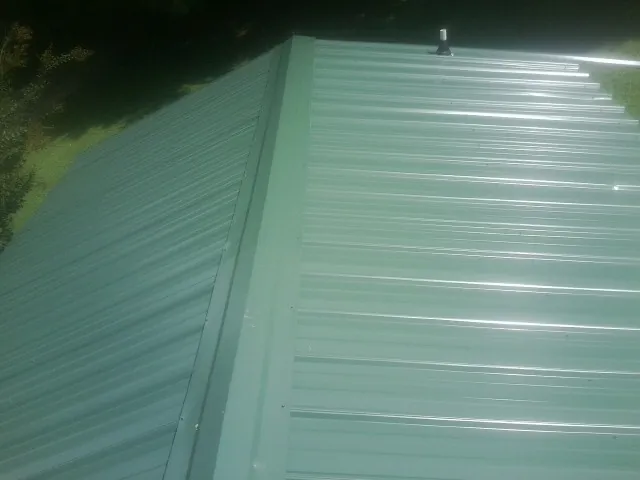 New green metal panels meeting at the ridge of a roof — Flat Roof Repair work by our crew in Mount Gilead